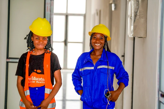 Two women in hard hats and workwear smiling